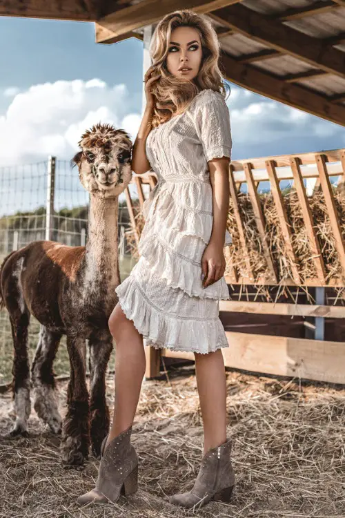 A woman wears cowboy boots with a tiered white dress