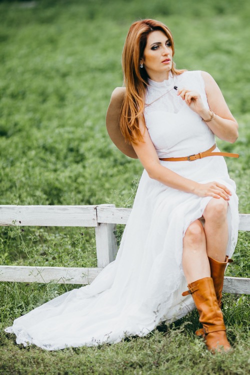 a woman wears cowboy boots with a white dress and a leather belt