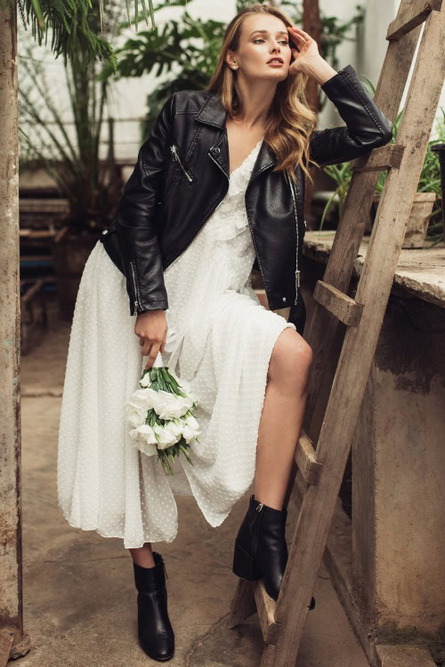 A woman wears cowboy boots with a white lace dress and a biker coat