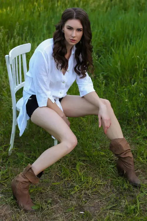 A woman wears cowboy boots with black shorts and a white shirts