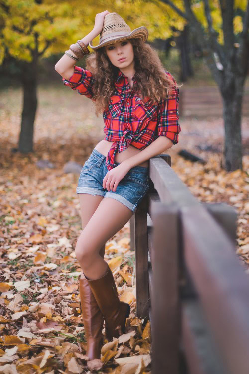A woman wears cowboy boots with denim shorts and a plaid shirt