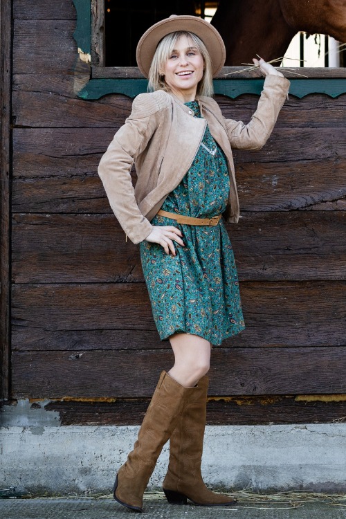 A woman wears cowboy boots with a floral dress and a coat
