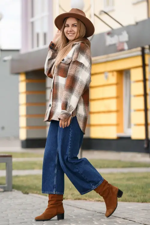 A woman wears cowboy boots with jeans and an oversized plaid shirt