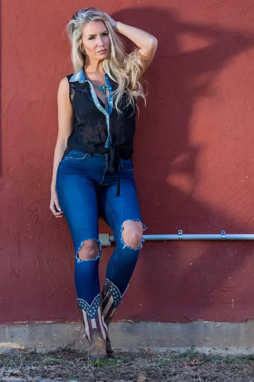 A woman wears cowboy boots with a ripped jeans and a vest