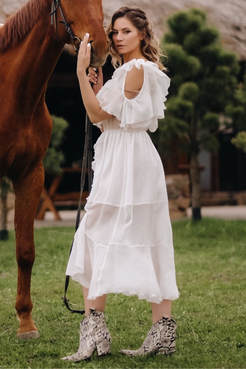 A woman wears a white dress with snakeskin cowboy boots
