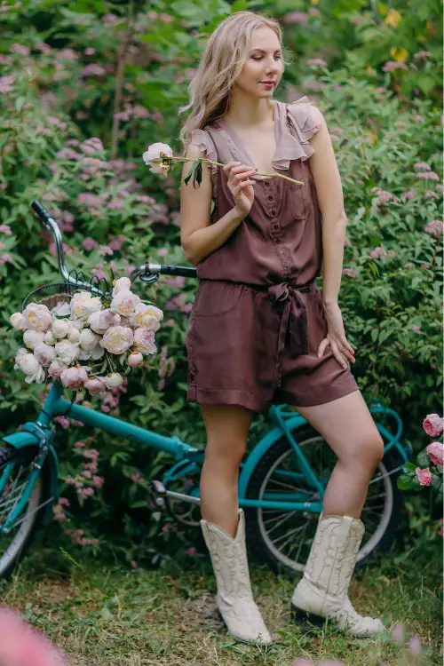 A woman wears cream cowboy boots with a roomper