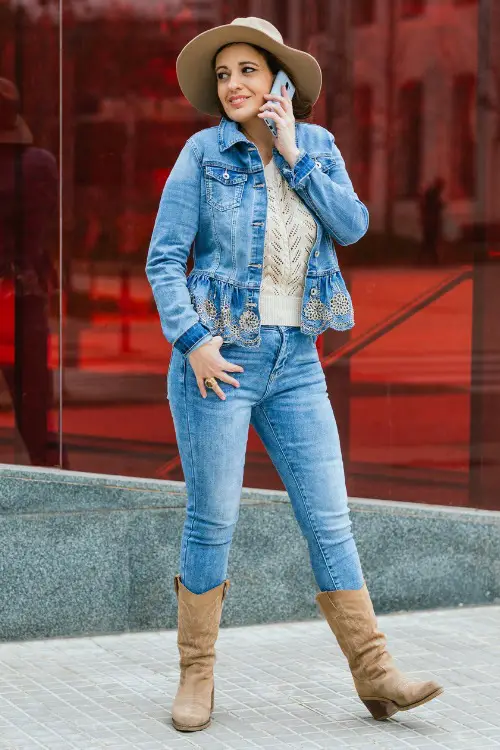 A woman wears jeasn, cowboy boots and a denim coat
