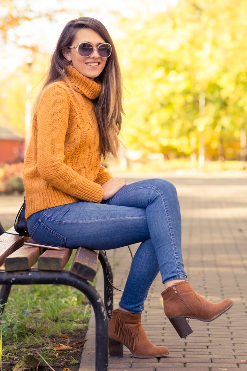 A woman wears orang sweater with jeans and a pair of cowboy boots