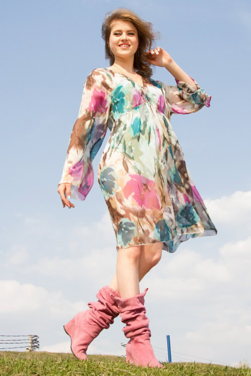 A woman wears pink cowboy boots with a colorful dress