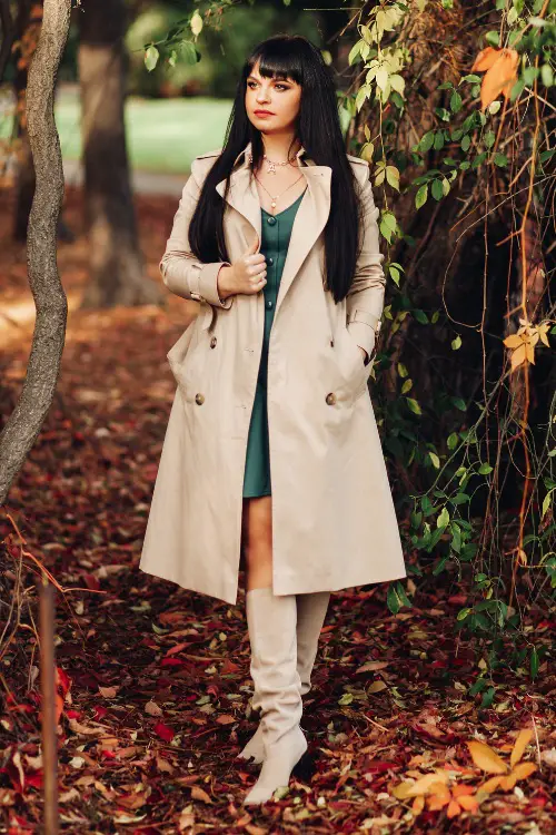 A woman wears white cowboy boots with a green dress and a long coat