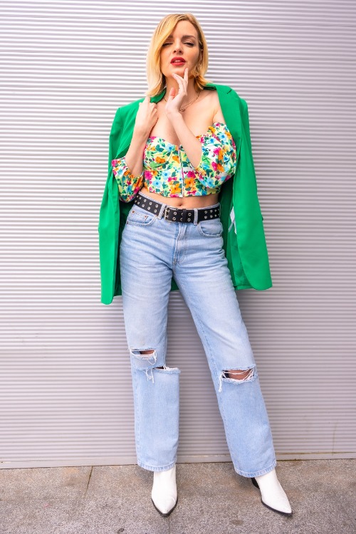 A woman wears white cowboy boots with ripped jeans, floral mini top and a green coat