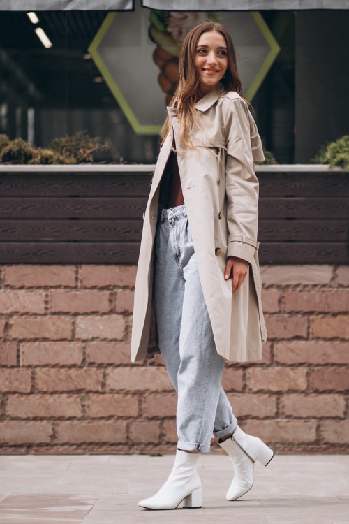 A woman wears white cowboy boots with jeans, long coat and simple tee