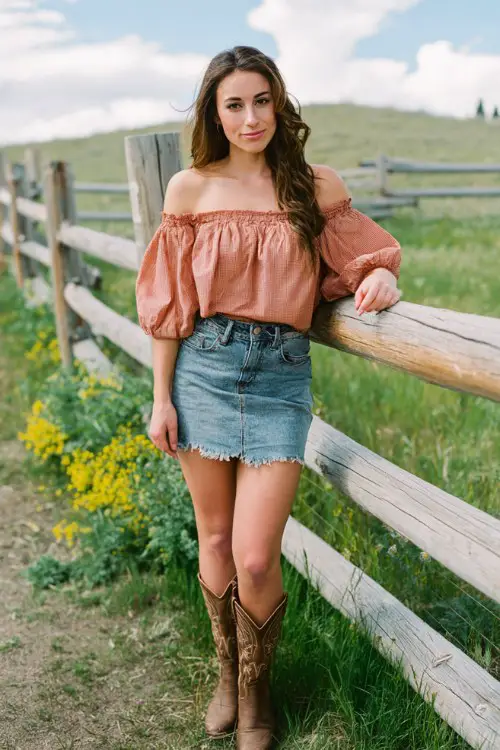 a woman wearing classic brown cowboy boots, a frayed denim mini skirt, and an off-shoulder peach top