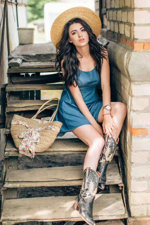 A woman wears a slip dress with a pair of cowboy boots