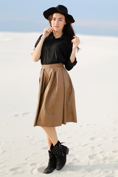 a woman wears black cowboy boots, black shirt, black hat and brown skirt