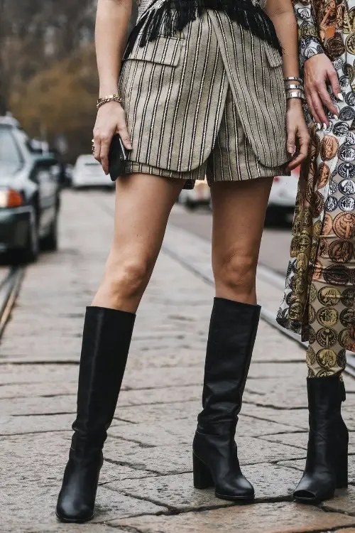 a woman wears black cowboy boots with blazer set with shorts