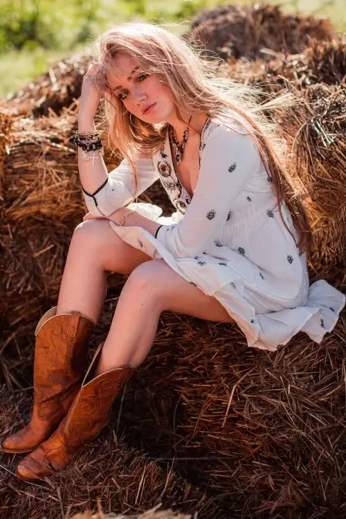 a woman wears brown cowboy boots with a white dress on the field