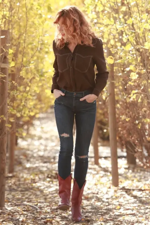 a woman wears brown cowboy boots with ripped jeans in the forest