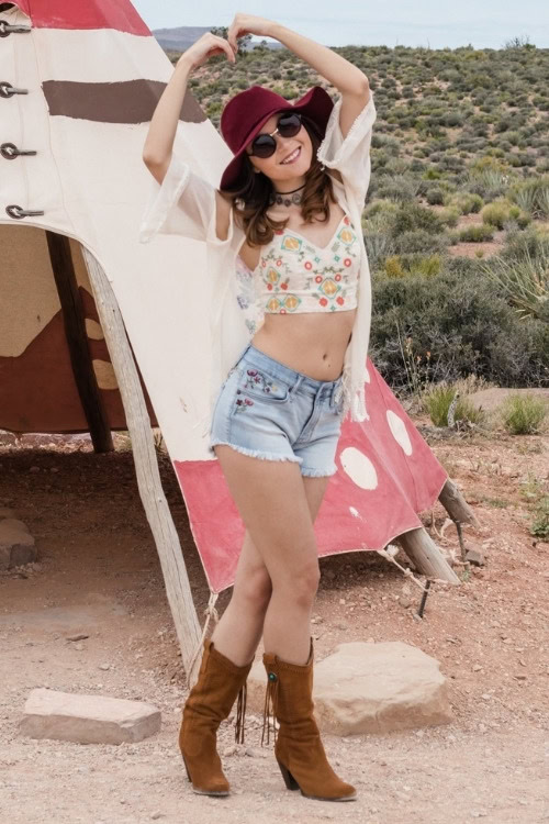 a woman wears brown cowboy boots with shorts and a floral top