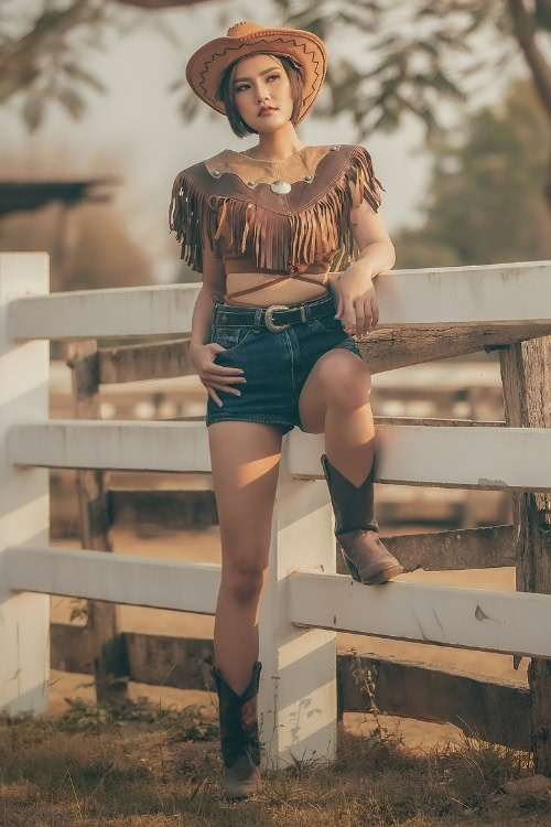 a woman wears brown cowboy boots with shorts and a fringe top