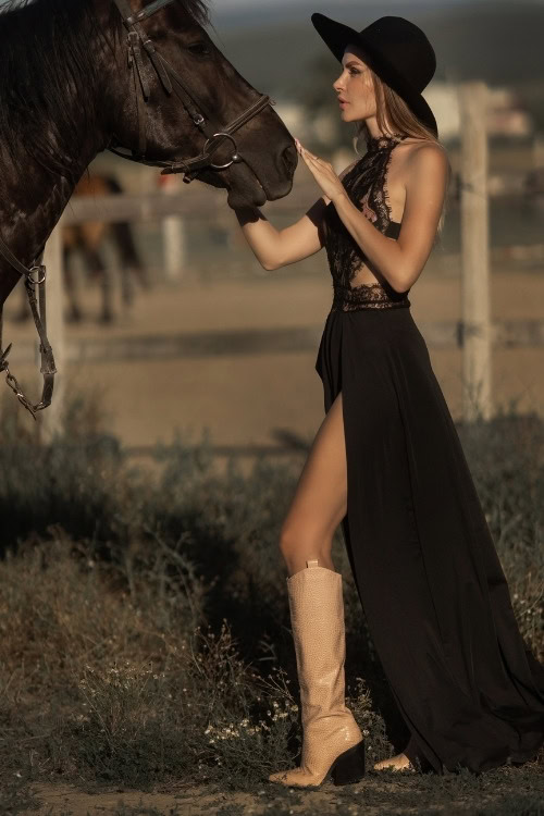 a woman wears cowboy boots with a black long slit dress