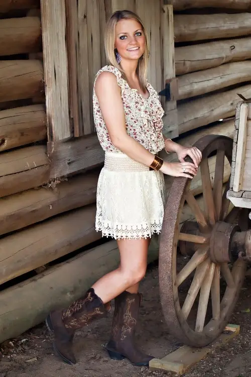 a woman wears cowboy boots with a lace skirt and a floral top