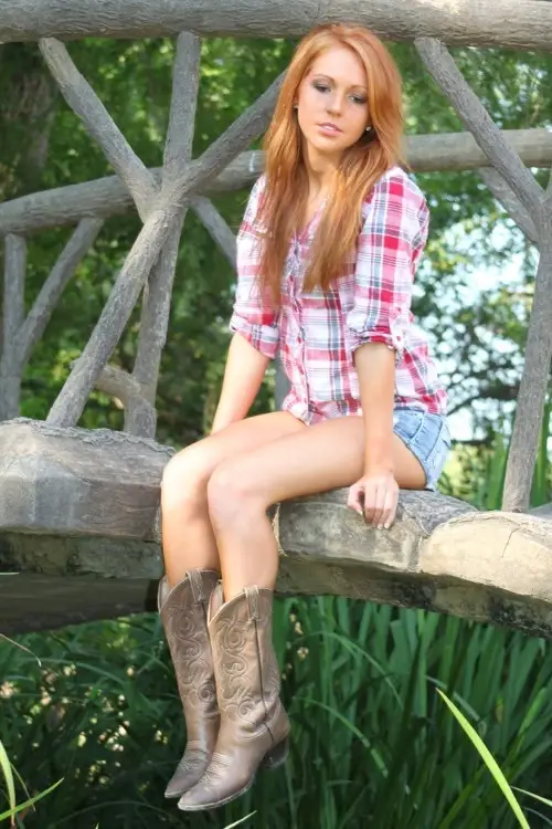 a woman wears cowboy boots with checkered shirt and denim shorts