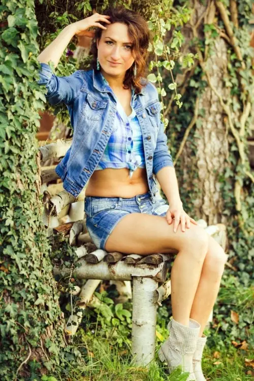 a woman wears cowboy boots with shorts and a denim jacket