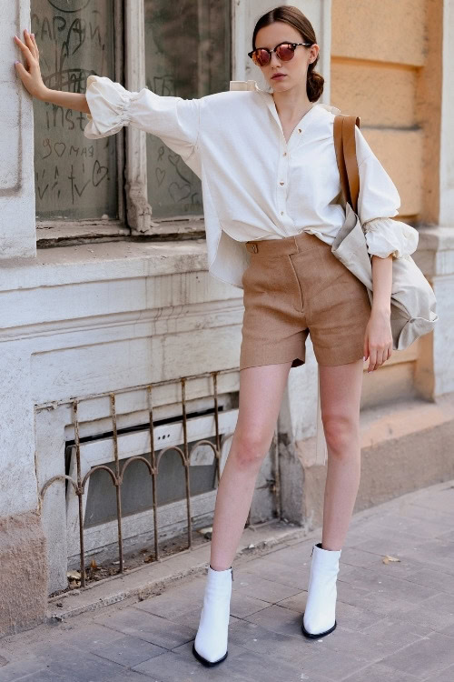 a woman wears white ankle cowboy boots with brown shorts and a white shirt