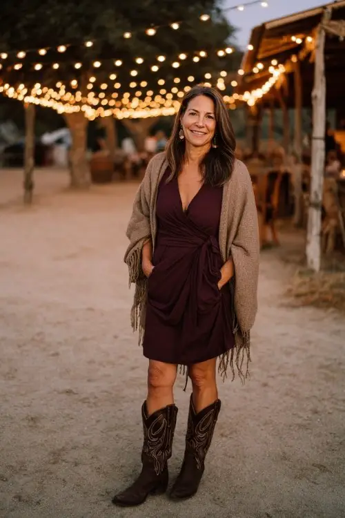 A woman over 40 wears a plum long-sleeve wrap dress with dark brown cowboy boots and a cashmere shawl