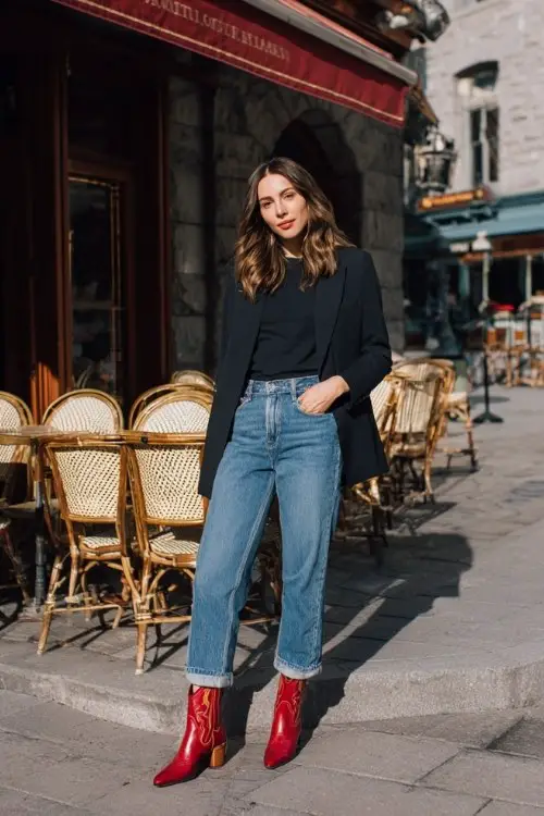 A woman wears red cowboy boots, high-waisted blue jeans, and a fitted black blazer