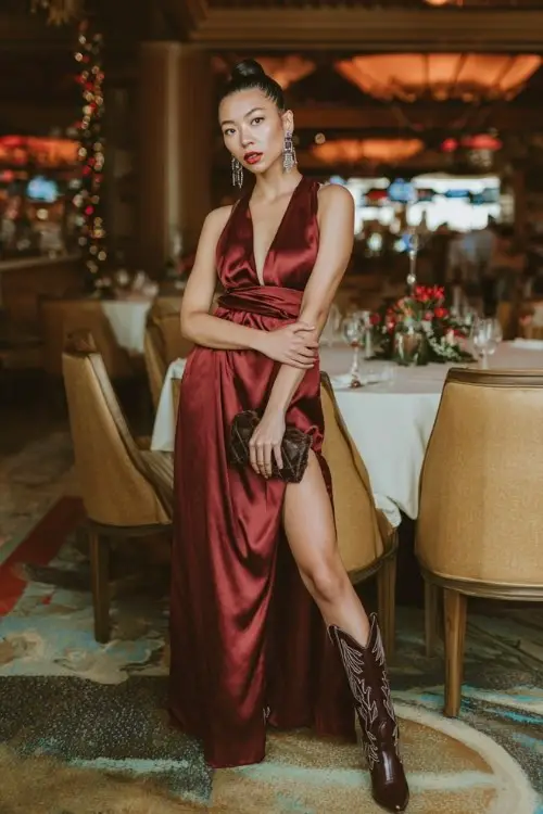 a woman wearing a long satin dress with a dramatic thigh-high slit and cowboy boots at a holiday dinner event