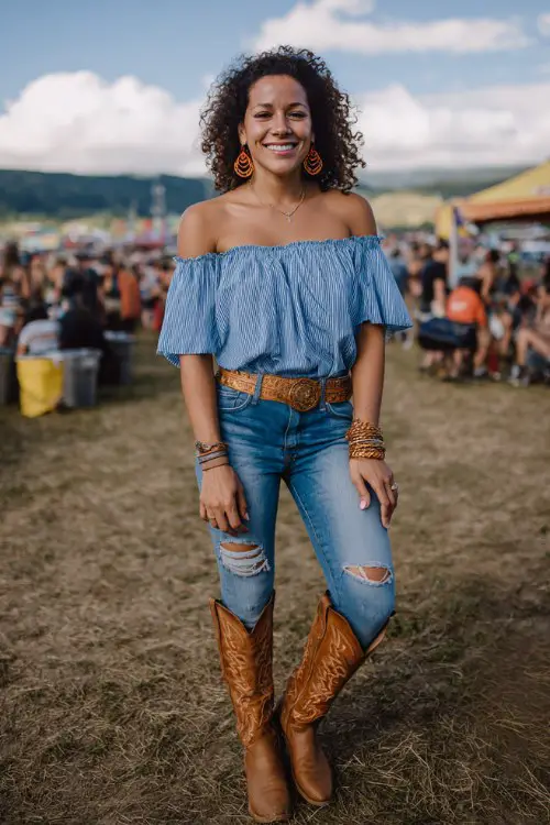 A curvy woman wears caramel cowboy boots with bootcut jeans, a breezy off-shoulder blouse and wide western belt, accessorized with statement earrings and bangles