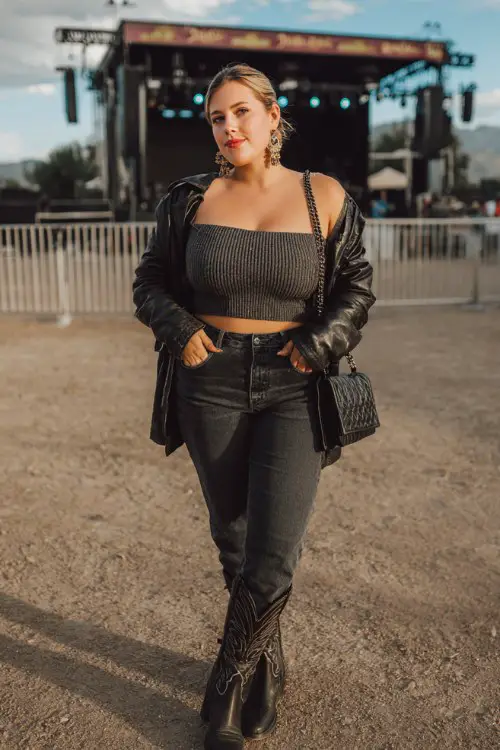 A plus-size woman wears black cowboy boots with tailored dark jeans, an off-shoulder knit top and cropped leather jacket, finished with statement earrings and mini shoulder bag