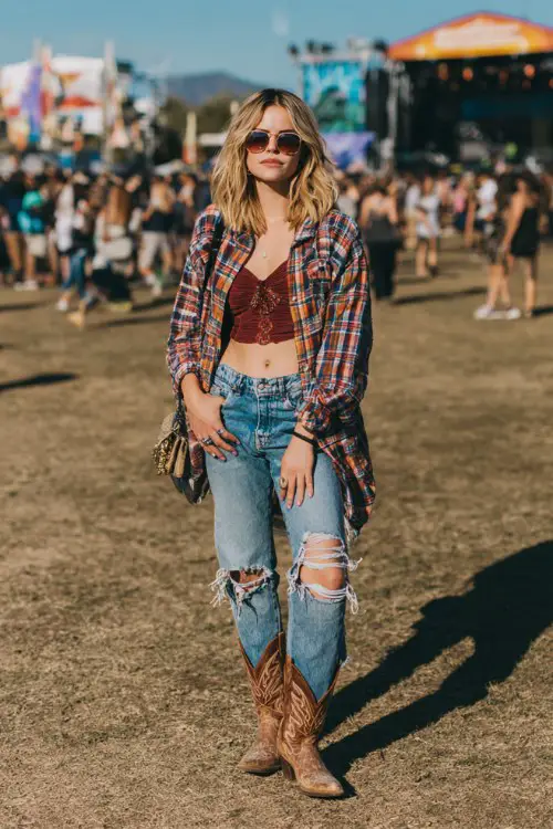 A woman wears embroidered brown cowboy boots with ripped boyfriend jeans, a fitted crop top and oversized flannel shirt