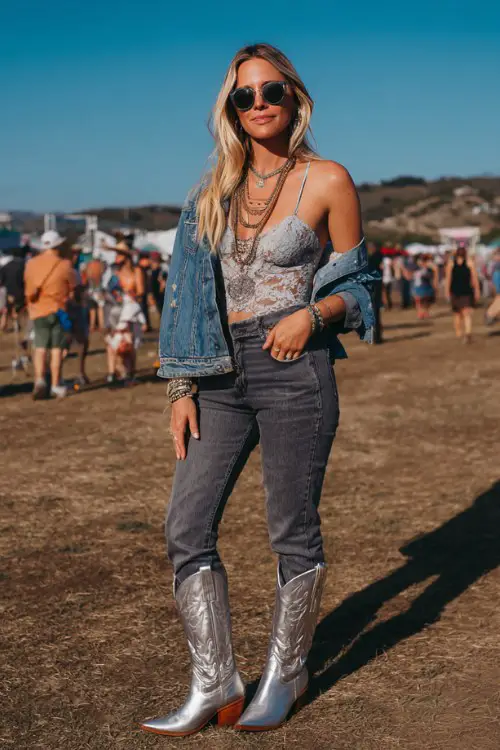 A woman wears metallic cowboy boots with high-rise jeans tucked in, a lace bodysuit and cropped denim jacket, accessorized with layered necklaces and sunglasses