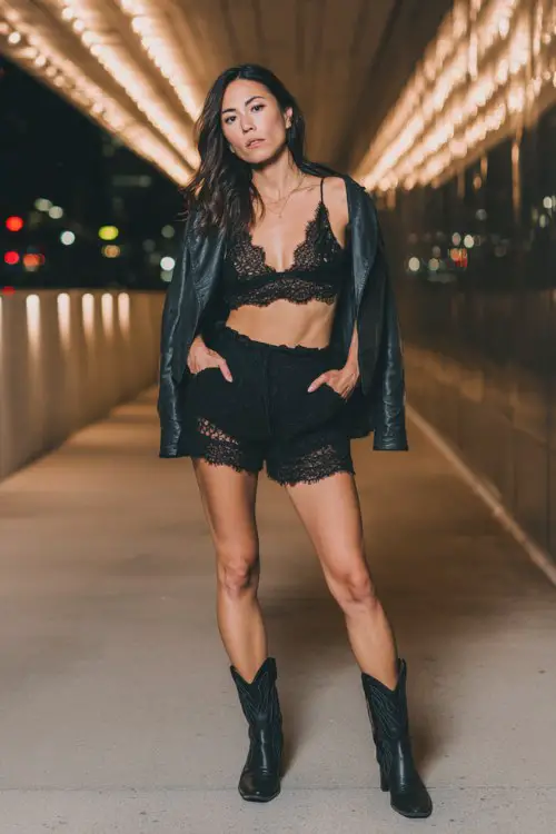 Woman in black lace bralette and lace shorts with black leather jacket, evening outdoor walkway with soft lights, confident stance