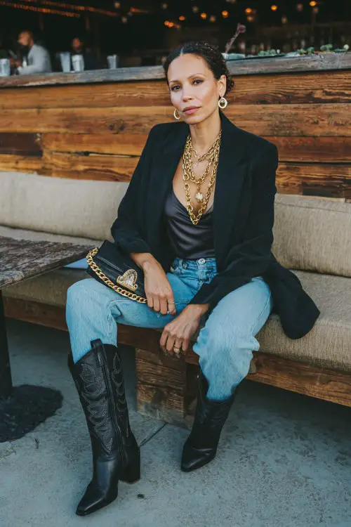 a woman wears a satin top with jeans, black cowboy boots