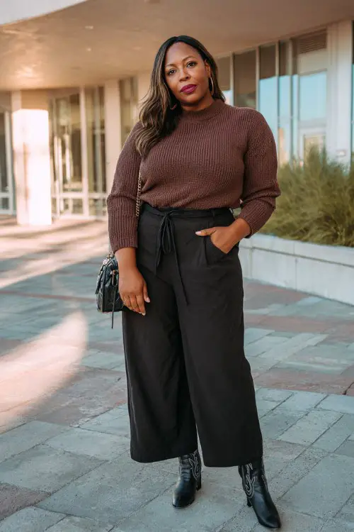 A curvy woman wears a fitted chocolate-brown sweater with black wide-leg trousers and black cowboy boots