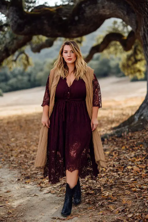 A plus-size woman wears a burgundy lace midi dress with sheer sleeves and black cowboy boots, layered with a camel wrap
