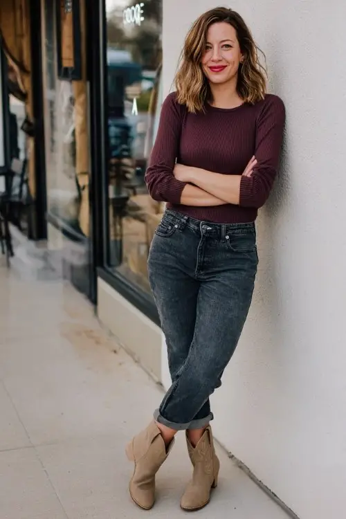 A woman wears dark denim skinny jeans with a tucked-in wine knit top and taupe short cowboy boots outfit for fall