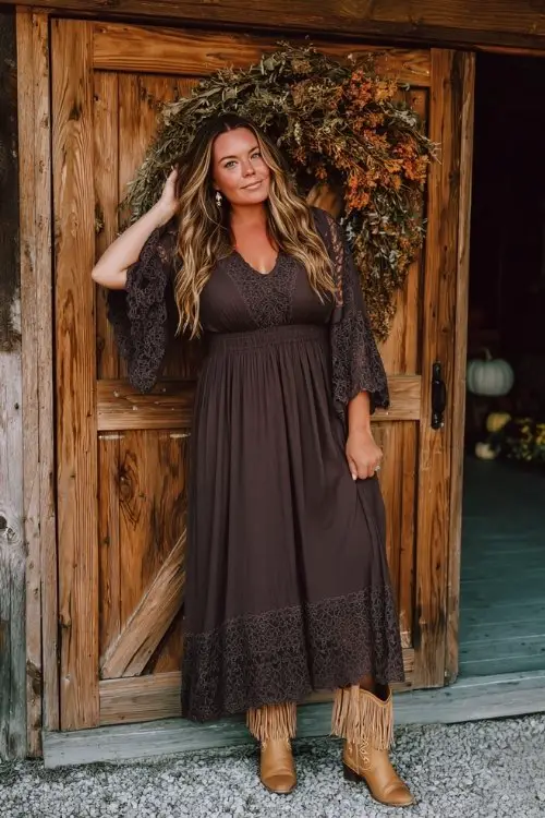 A curvy woman in a chocolate brown boho maxi dress with lace panels and bell sleeves, paired with tan fringe cowboy boots