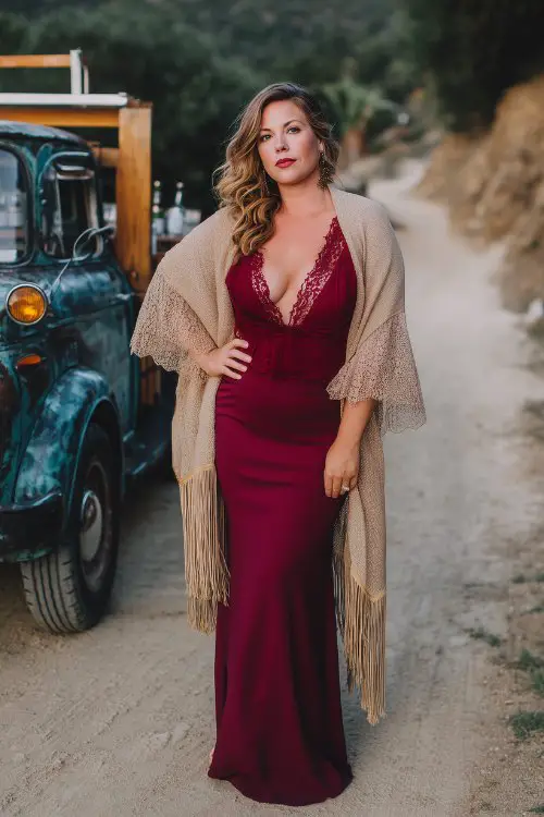 A curvy woman in a wine red boho dress with lace insets and bell sleeves, wrapped in a soft beige fringe shaw