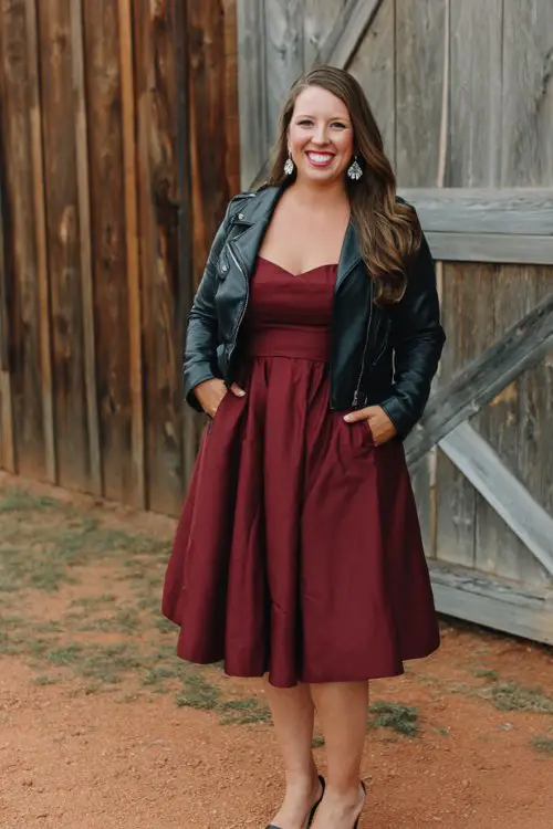 A curvy woman wears a burgundy fit-and-flare dress styled with a black leather jacket
