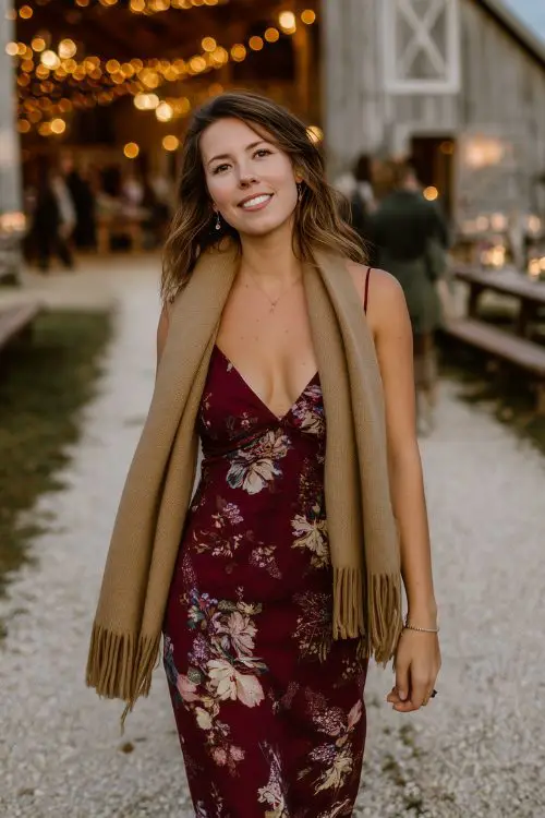A curvy woman wears a deep burgundy floral slip dress layered with a tan wool scarf tied loosely around her neck