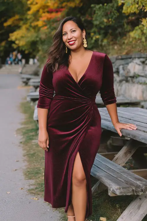 A curvy woman wears a maroon wrap-style velvet dress with a side slit and subtle shimmer