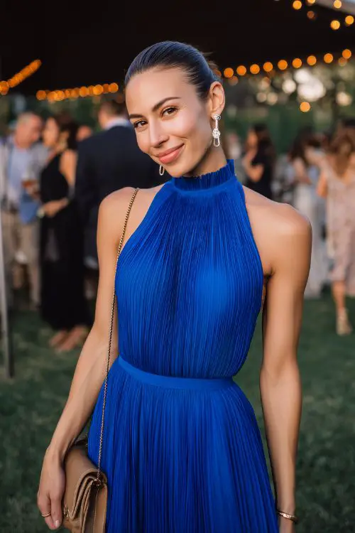 A guest in a royal blue pleated midi dress with a high neck and open back,