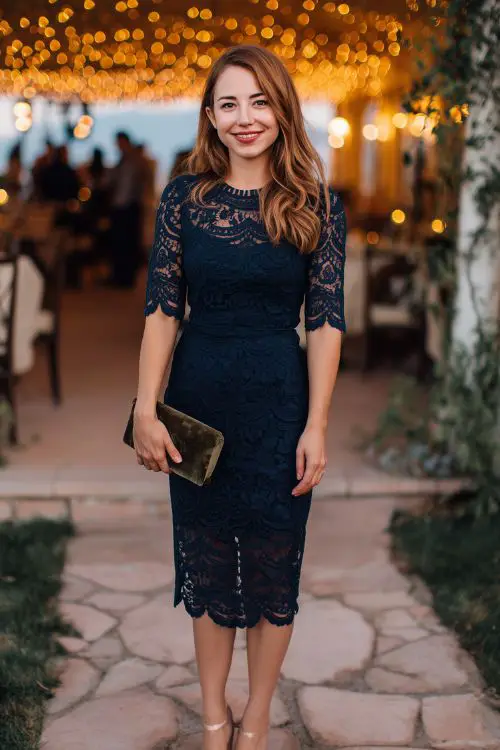 A midsize woman in a navy lace midi dress with scalloped edges and ¾ sleeves, paired with heels and a velvet clutch