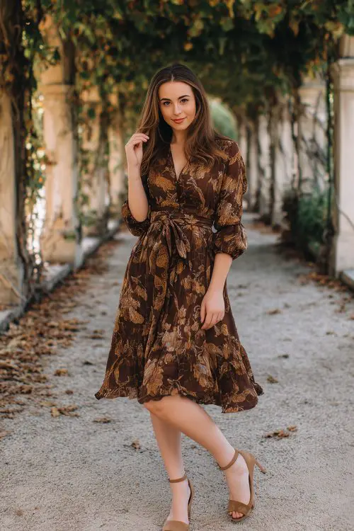 A petite woman in a chocolate brown floral-print tea dress with a belted waist and low heels,