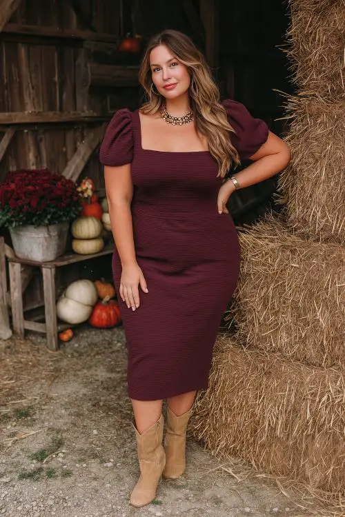 A plus size guest in a fitted maroon midi dress with a square neckline and puff sleeves, paired with tan boots and a statement necklace